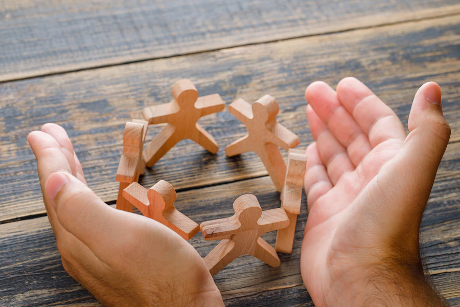 business-success-concept-wooden-table-top-view-hands-protecting-wooden-figures-people_176474-9273